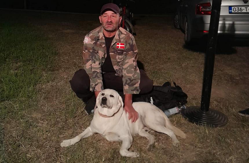 Čovjek u maskirnoj košulji iza psa, ljubimca, kojeg drži rukama.